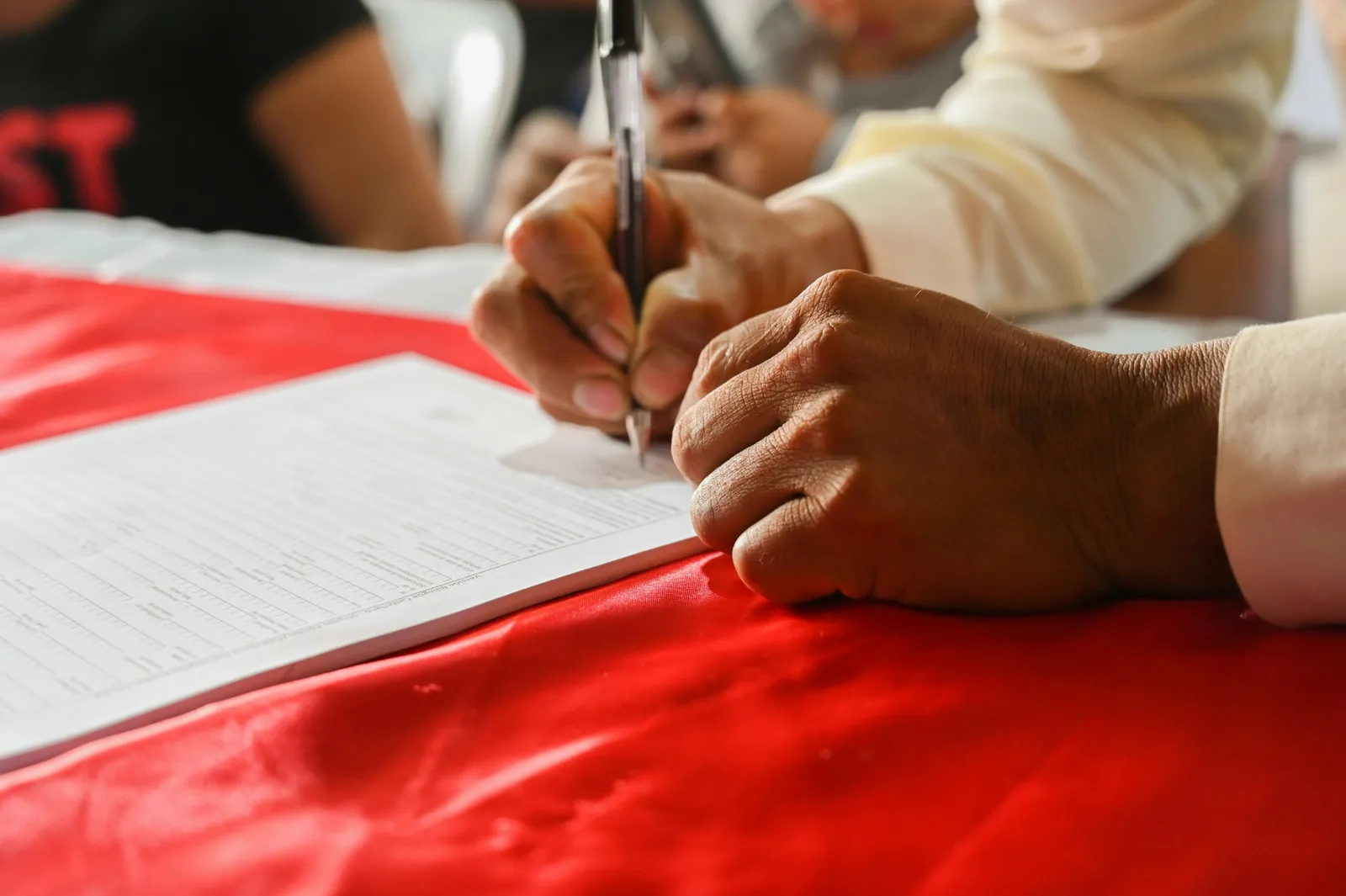Main qui signe un document posé sur une nappe rouge